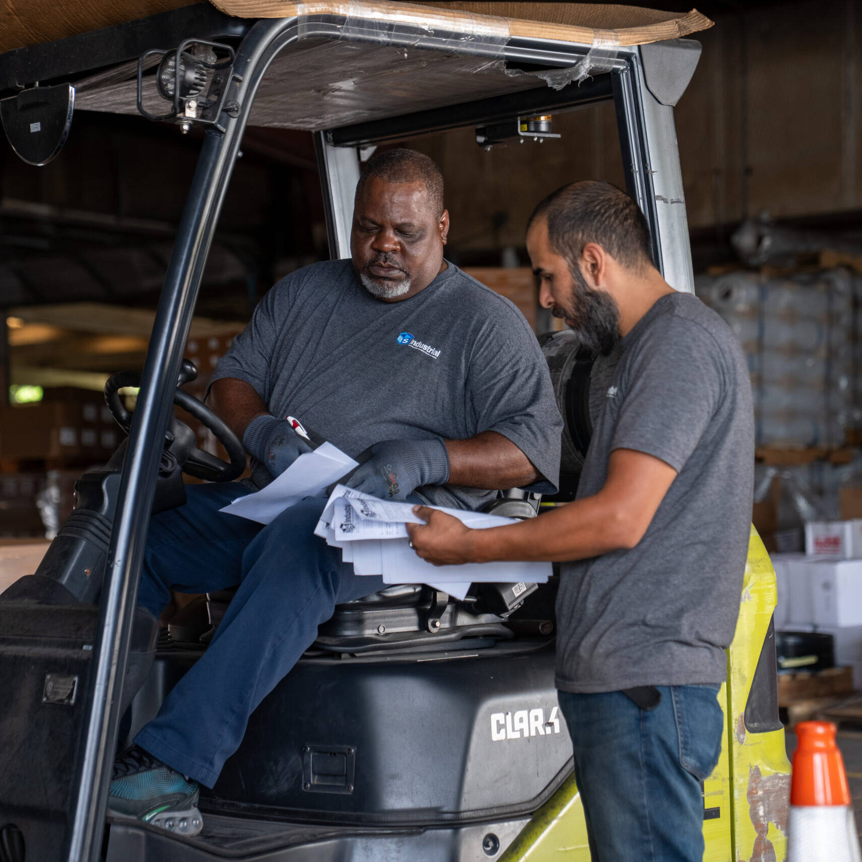 two warehouse employees work together next to forklift